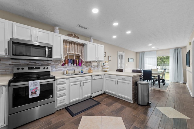 kitchen with stainless steel appliances, kitchen peninsula, a textured ceiling, dark hardwood / wood-style floors, and white cabinetry