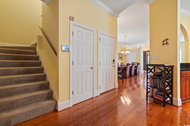 foyer entrance featuring ornamental molding, a chandelier, stairway, arched walkways, and wood finished floors
