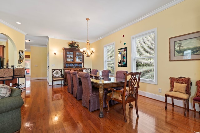 dining room featuring crown molding, arched walkways, a notable chandelier, and wood finished floors