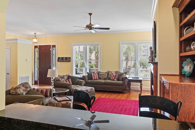 living area featuring wood finished floors, ceiling fan, ornamental molding, and visible vents