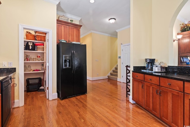 kitchen with dark stone countertops, arched walkways, light wood-type flooring, crown molding, and black appliances