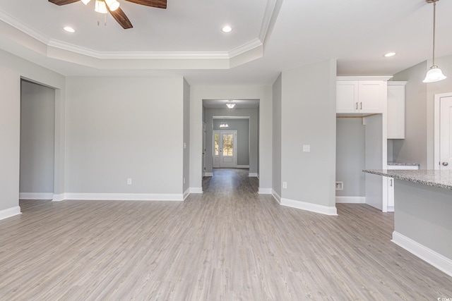 unfurnished living room featuring ceiling fan, crown molding, a tray ceiling, and light hardwood / wood-style flooring