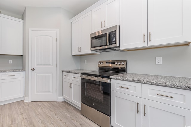 kitchen with light stone counters, white cabinetry, stainless steel appliances, and light hardwood / wood-style flooring