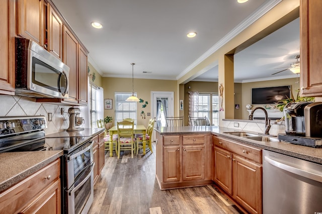 kitchen with stainless steel appliances, sink, light hardwood / wood-style floors, kitchen peninsula, and hanging light fixtures