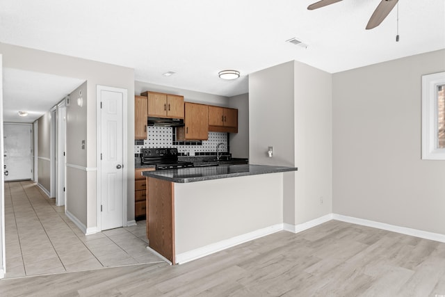 kitchen featuring black stove, tasteful backsplash, kitchen peninsula, dark stone countertops, and light wood-type flooring