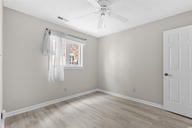 empty room with ceiling fan, light wood-type flooring, and a textured ceiling