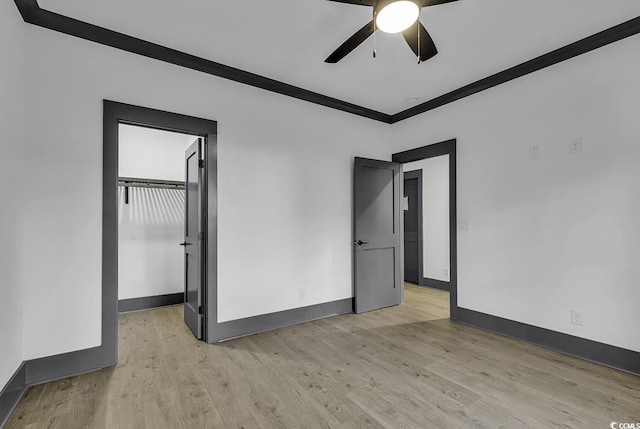 unfurnished bedroom with ceiling fan, light hardwood / wood-style floors, ornamental molding, and a walk in closet