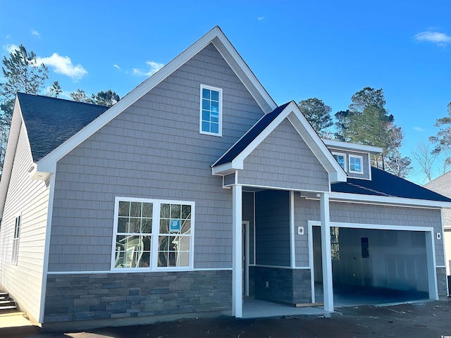 view of front facade with a garage, stone siding, and a shingled roof