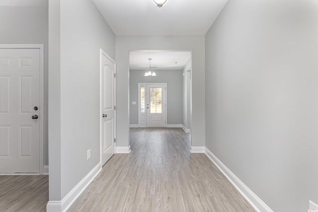 entryway featuring light wood-type flooring, an inviting chandelier, and baseboards