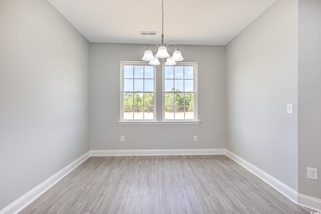 empty room with baseboards, light wood-style flooring, visible vents, and a notable chandelier