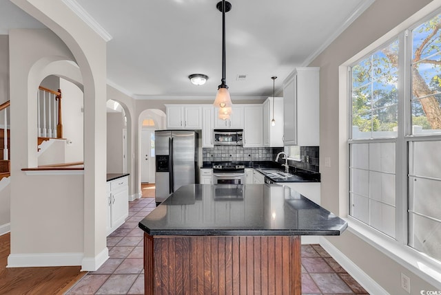 kitchen featuring white cabinets, appliances with stainless steel finishes, decorative light fixtures, and a kitchen island