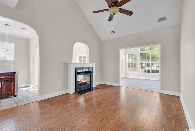 unfurnished living room with ceiling fan, a multi sided fireplace, light hardwood / wood-style floors, and high vaulted ceiling