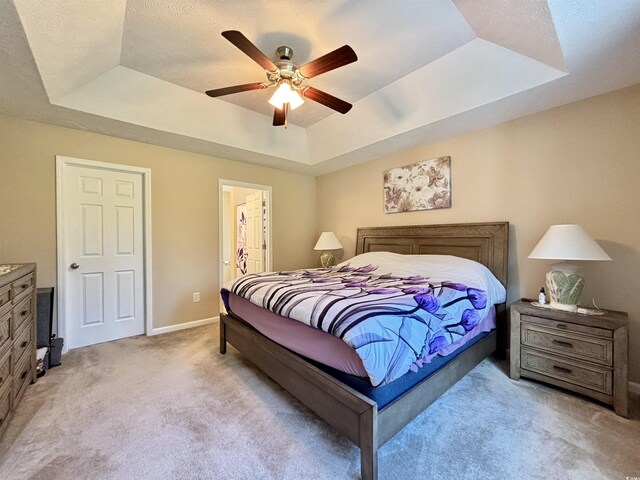 bedroom featuring connected bathroom, light carpet, a tray ceiling, and ceiling fan