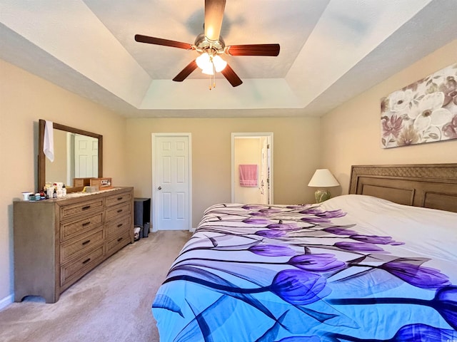 carpeted bedroom featuring ceiling fan, a raised ceiling, and ensuite bath