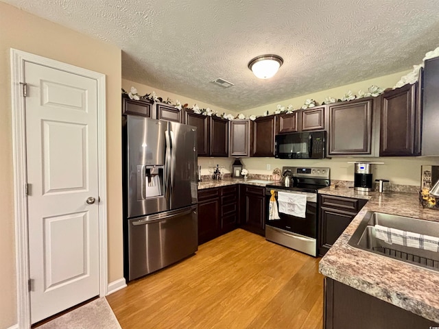 kitchen with appliances with stainless steel finishes, a textured ceiling, dark brown cabinets, and light hardwood / wood-style floors