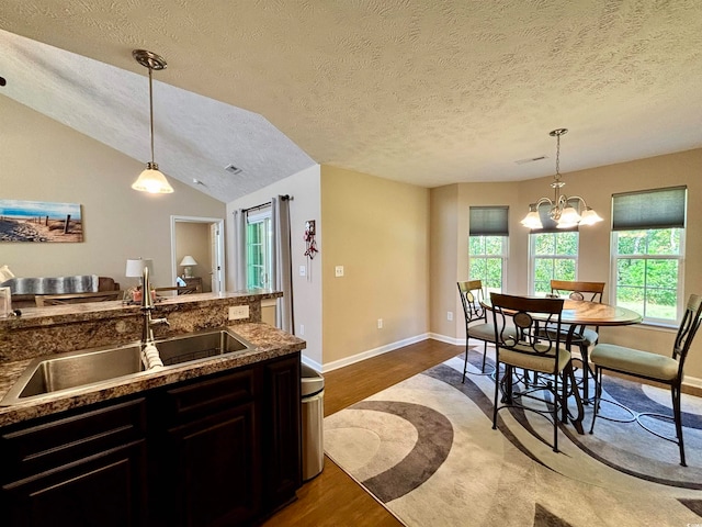 kitchen with sink, light wood-type flooring, a textured ceiling, vaulted ceiling, and decorative light fixtures