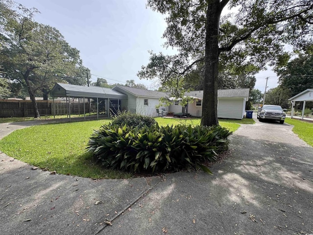 ranch-style house with a front yard, a detached carport, driveway, and fence