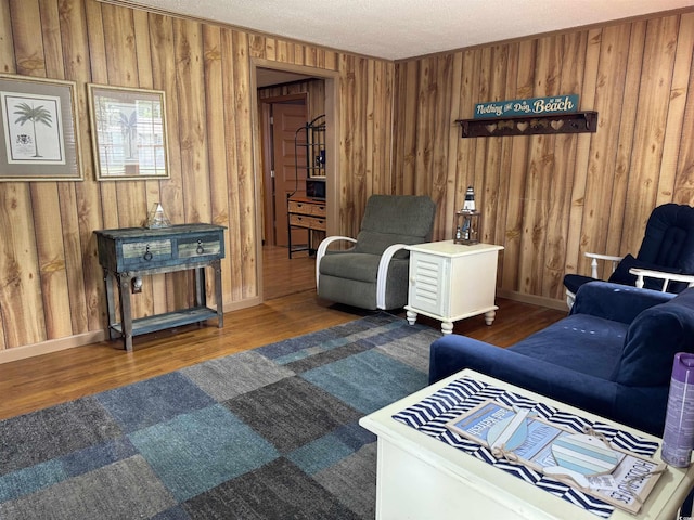 living room with wooden walls, a textured ceiling, baseboards, and wood finished floors