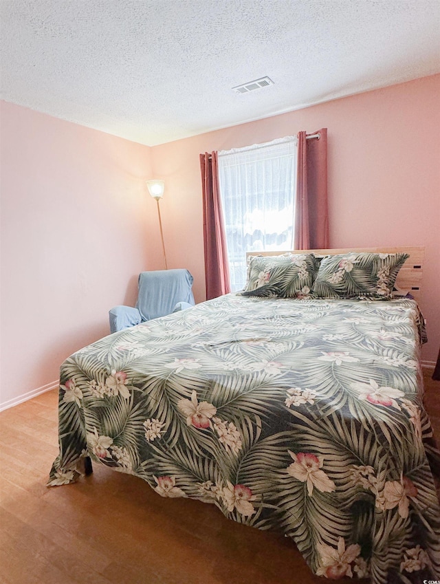 bedroom featuring visible vents, baseboards, a textured ceiling, and wood finished floors