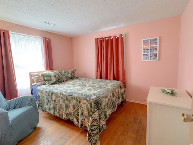 bedroom with visible vents, baseboards, a textured ceiling, and wood finished floors