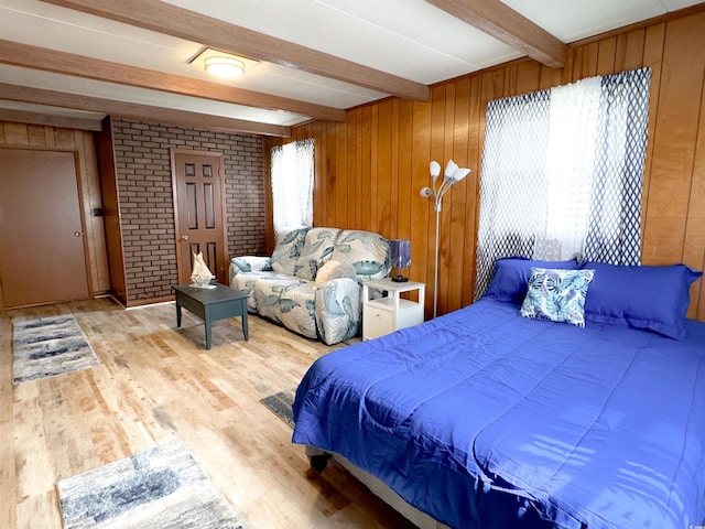 bedroom with light wood finished floors, beam ceiling, and wood walls