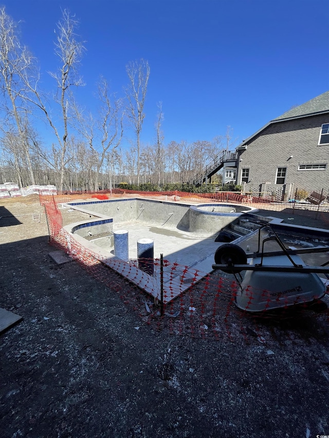 view of swimming pool featuring a hot tub, fence, and an empty pool