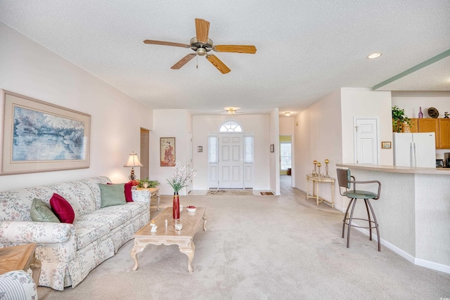 living area featuring a textured ceiling, a ceiling fan, light carpet, and baseboards