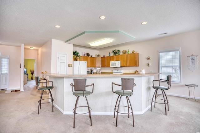 kitchen featuring white appliances, light carpet, a textured ceiling, a breakfast bar, and plenty of natural light