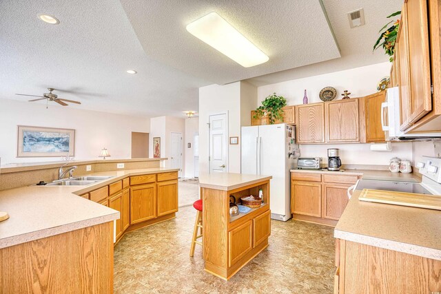 kitchen with white appliances, a sink, a textured ceiling, a kitchen island, and light countertops