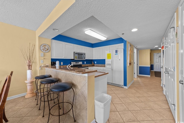 kitchen with kitchen peninsula, a kitchen bar, a textured ceiling, stainless steel appliances, and white cabinetry