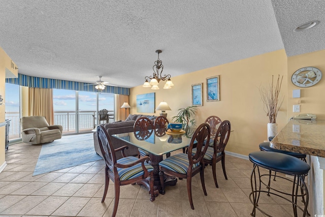 tiled dining area featuring ceiling fan with notable chandelier, a water view, and a textured ceiling