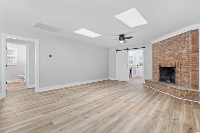 unfurnished living room featuring a healthy amount of sunlight, a skylight, ceiling fan, a barn door, and light hardwood / wood-style floors