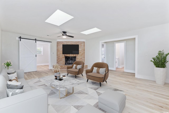 living room featuring a barn door, ceiling fan, light hardwood / wood-style flooring, and a brick fireplace