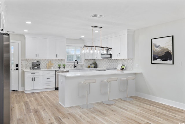 kitchen featuring white cabinets, hanging light fixtures, a kitchen bar, kitchen peninsula, and stainless steel appliances