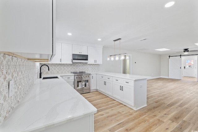 kitchen featuring white cabinetry, sink, a barn door, decorative light fixtures, and range with two ovens