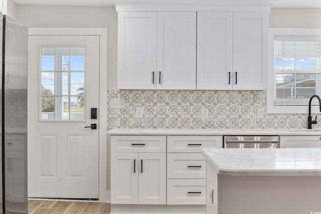 kitchen with tasteful backsplash, light hardwood / wood-style flooring, white cabinets, and stainless steel dishwasher