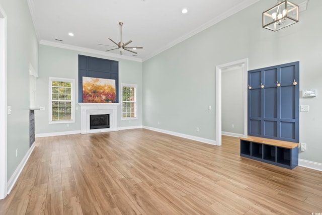 unfurnished living room featuring baseboards, crown molding, light wood-type flooring, a fireplace, and ceiling fan with notable chandelier