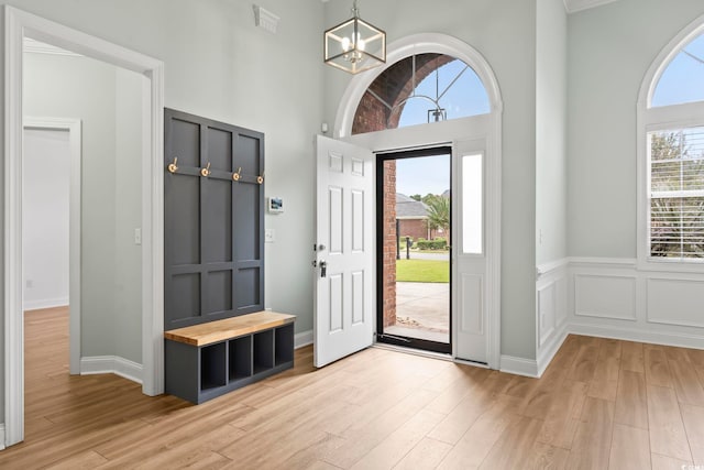 foyer with a towering ceiling, light wood-style floors, visible vents, and a chandelier