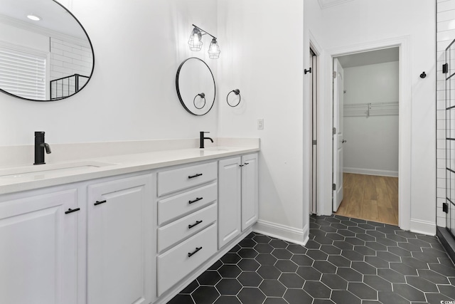 full bathroom with double vanity, baseboards, tile patterned flooring, a walk in closet, and a sink