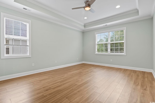 empty room with light wood-type flooring, baseboards, visible vents, and a raised ceiling