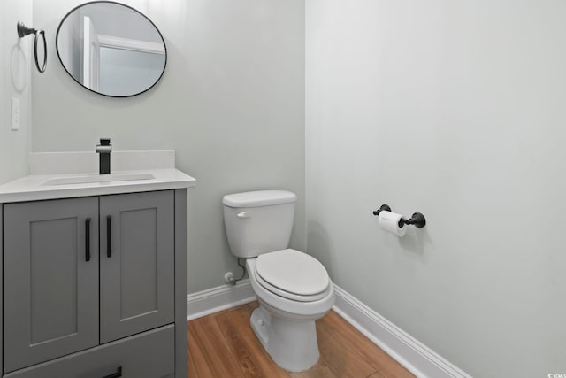 half bath featuring baseboards, vanity, toilet, and wood finished floors