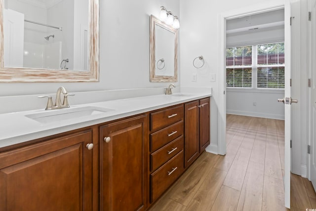 full bath with double vanity, a sink, baseboards, and wood finished floors