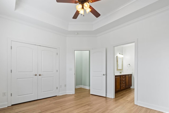 unfurnished bedroom featuring a closet, baseboards, light wood-style flooring, a tray ceiling, and a sink