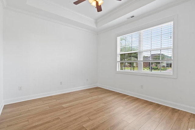 spare room with ornamental molding, light wood-type flooring, a raised ceiling, and baseboards