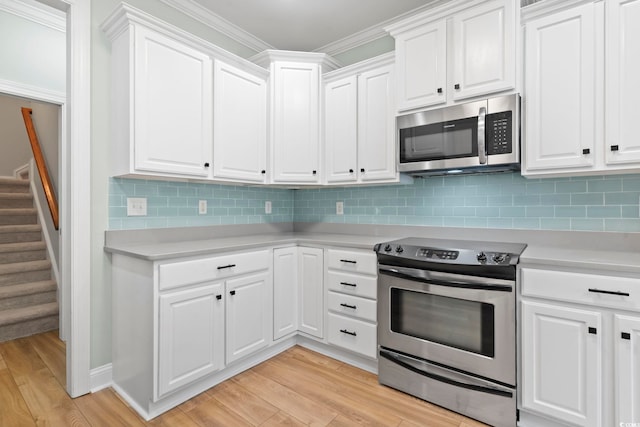 kitchen featuring light wood finished floors, white cabinets, appliances with stainless steel finishes, ornamental molding, and light countertops