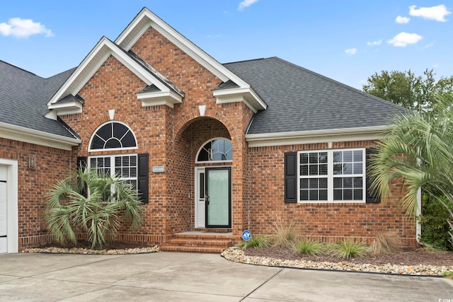 traditional-style house featuring a shingled roof, concrete driveway, and brick siding