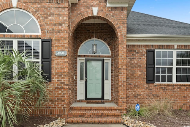 view of exterior entry with roof with shingles and brick siding