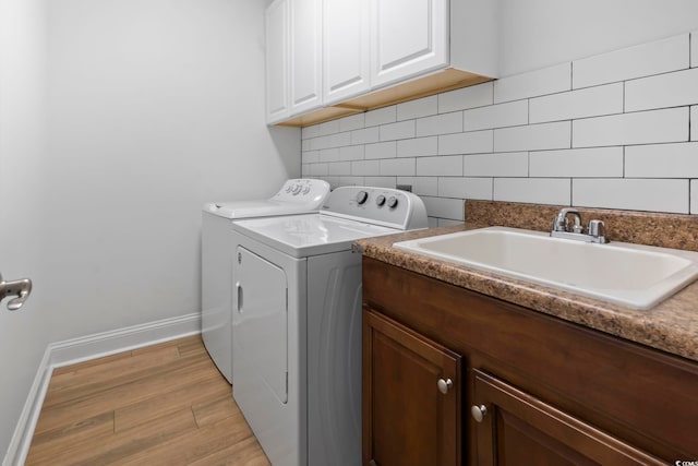 washroom featuring a sink, baseboards, light wood-type flooring, independent washer and dryer, and cabinet space