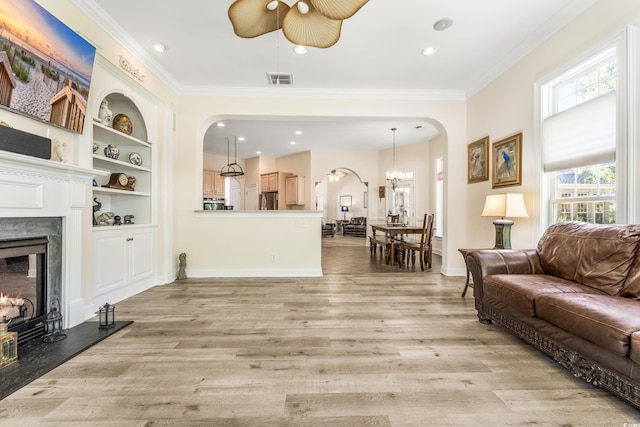 living room featuring ceiling fan with notable chandelier, light wood-type flooring, a premium fireplace, and ornamental molding