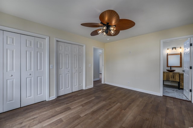 unfurnished bedroom with ensuite bath, ceiling fan, wood-type flooring, and two closets